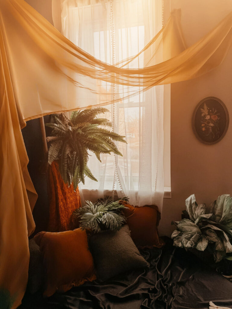 Cozy room with plants, pillows, and draped curtains.
